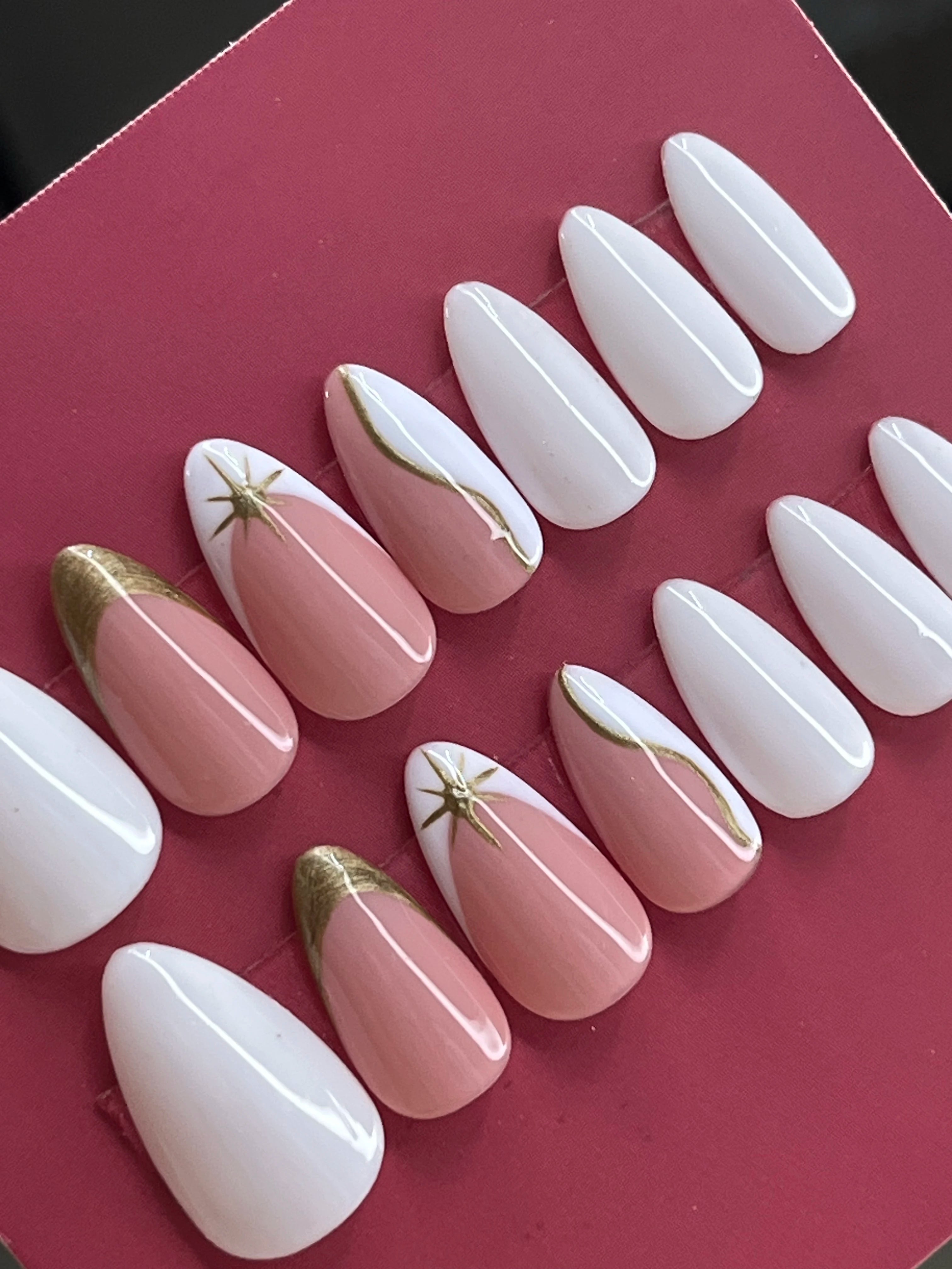 Set of 24 universal size white and pink artificial nails with gold accents on a red background