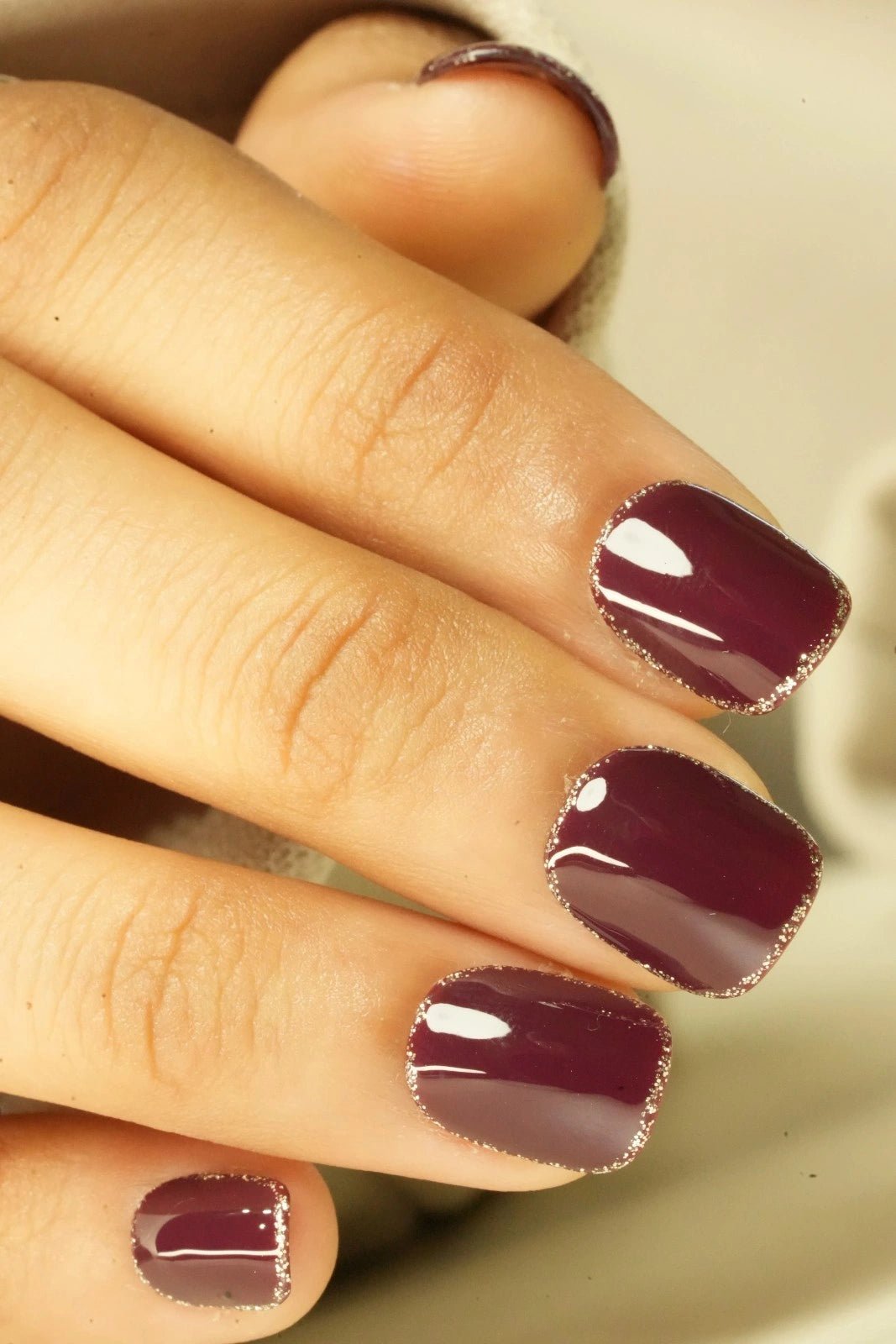 Close-up of a hand with maroon red fake nail on a neutral background
