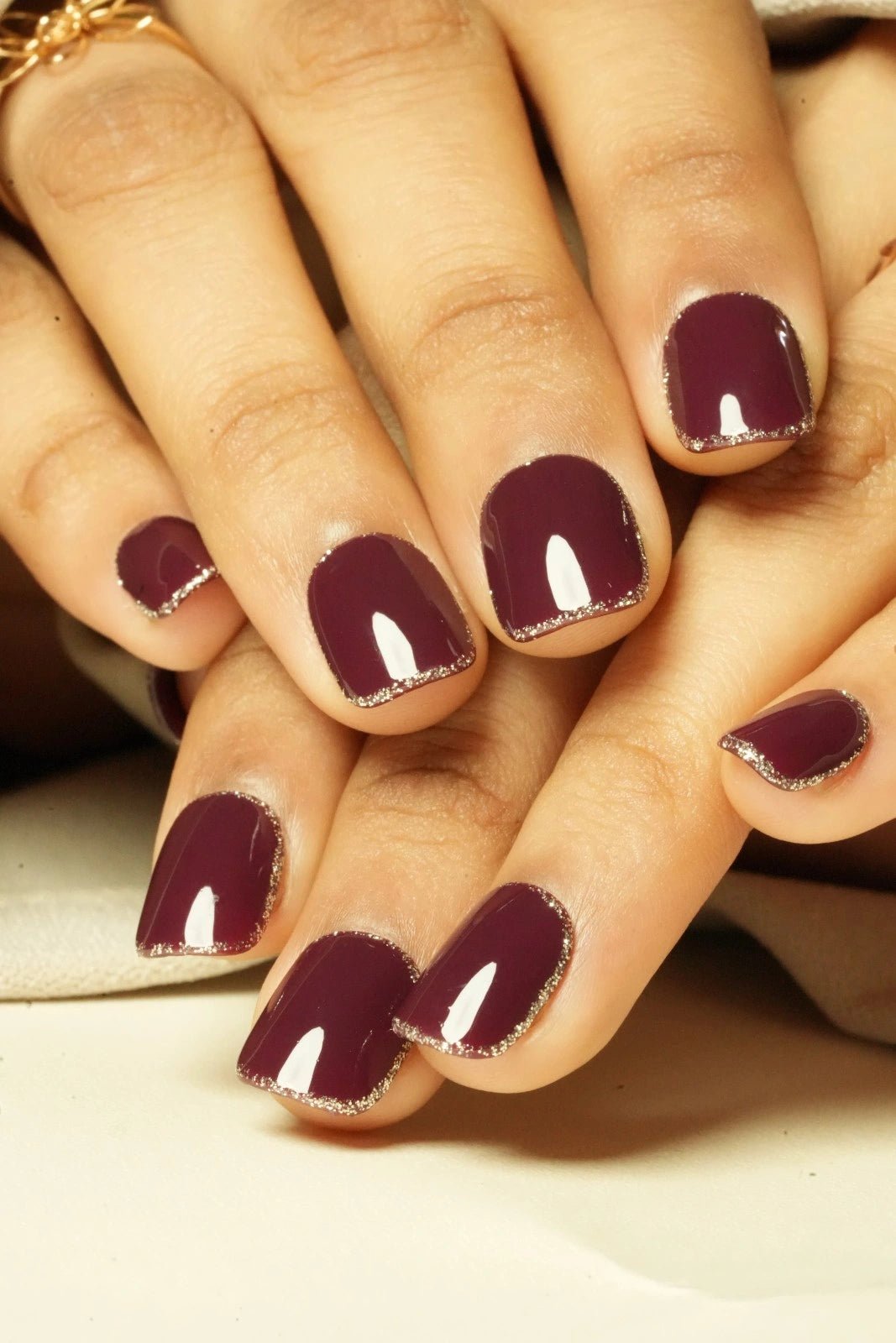 Close-up of hands with burgundy maroon red press on nail on a neutral background
