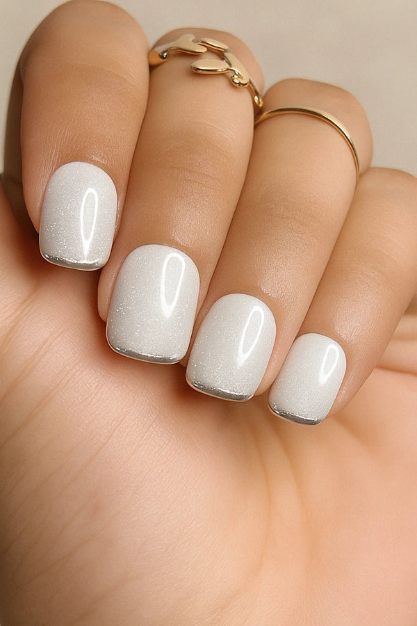 Close-up of a hand with white glitter nails with a silver french and gold rings on a neutral background