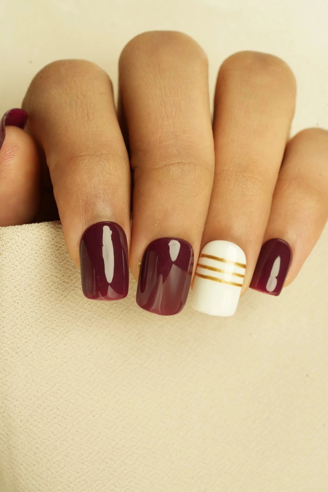 Close-up of a hand with buy maroon red short square soft gel press on nails
 on a beige background