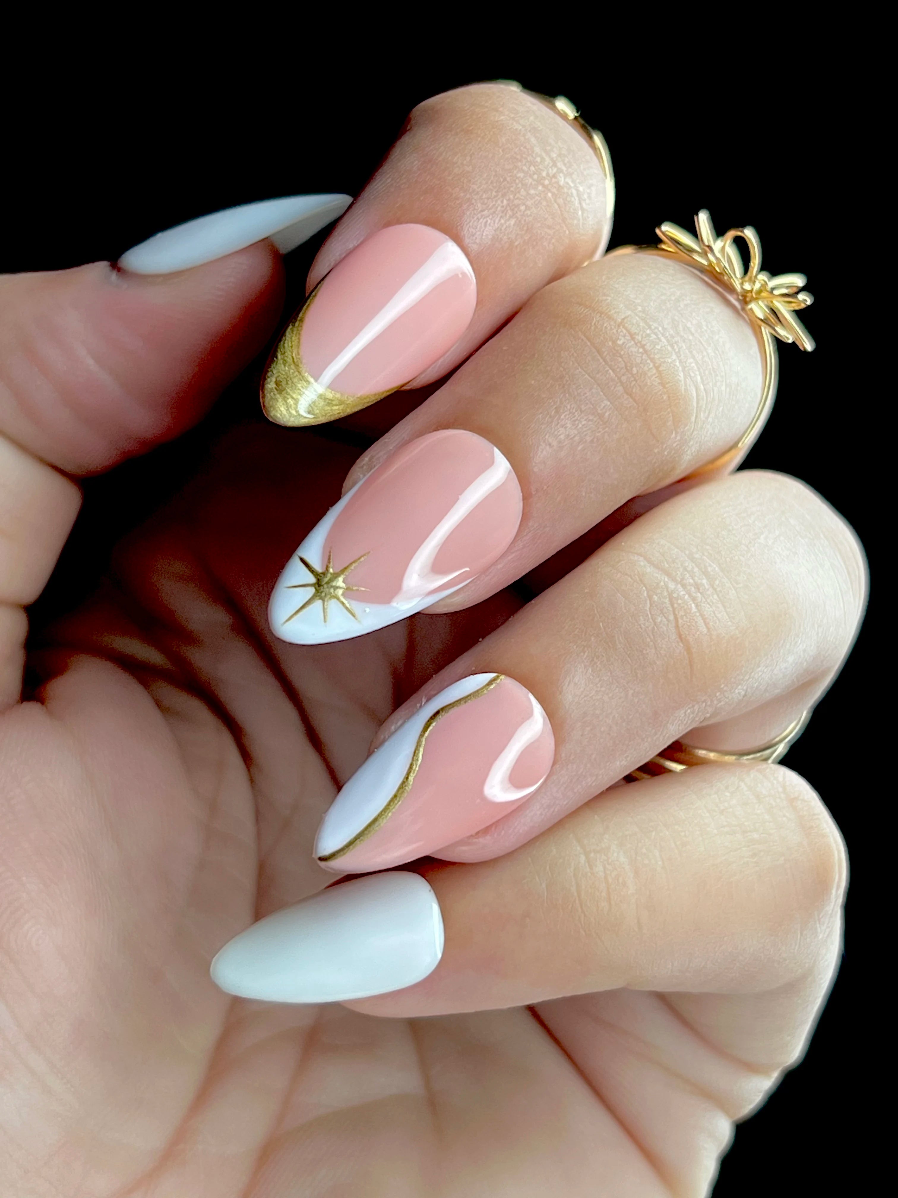 Hand with pink and white almond nails featuring gold accents french on a black background