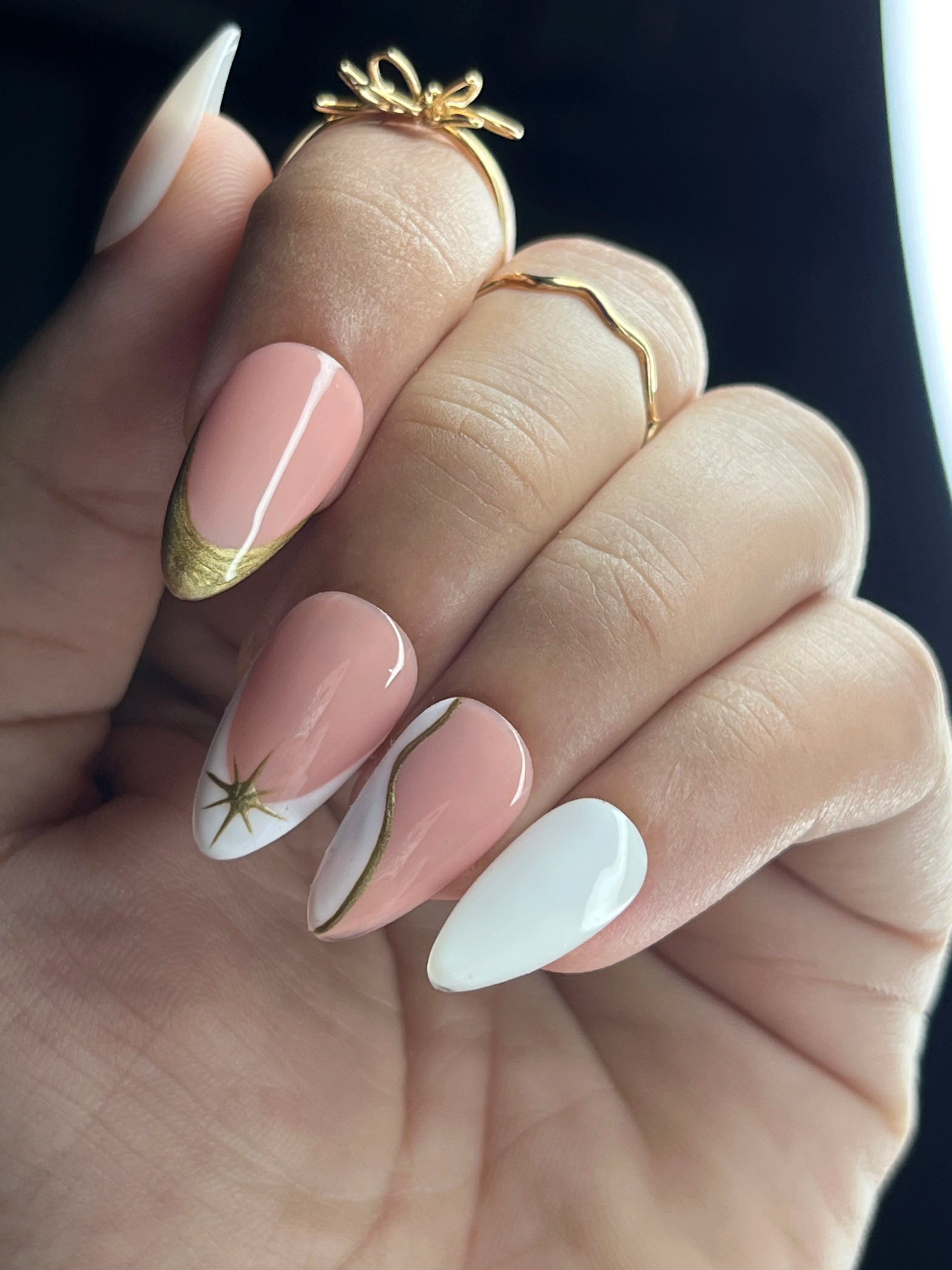 Hand with pink and white nails and gold rings on a dark background
