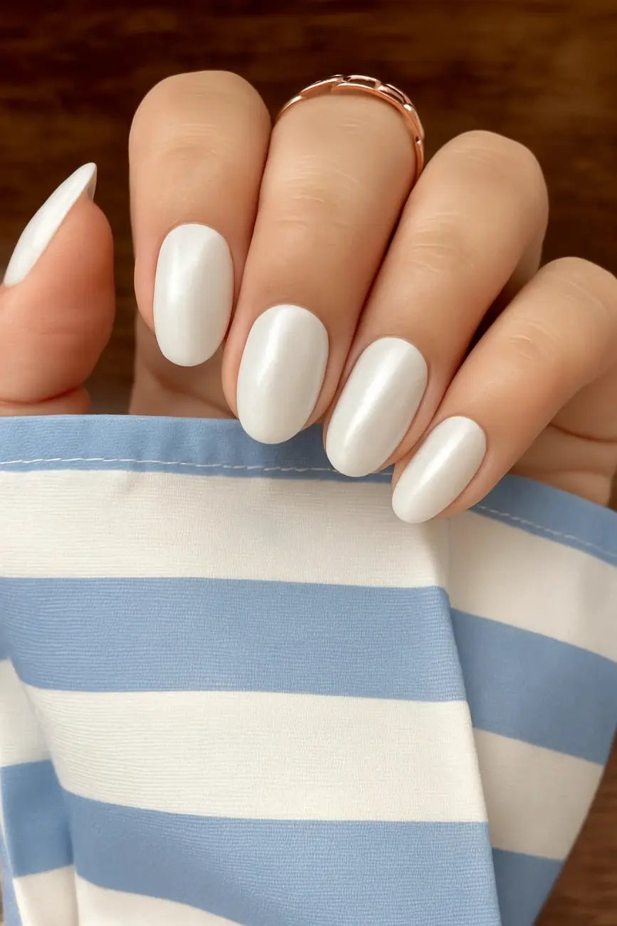 Close-up of a hand with white nail polish wearing a gold ring, against a blurred background. You will get 24 white silver chrome fake nails in this kit