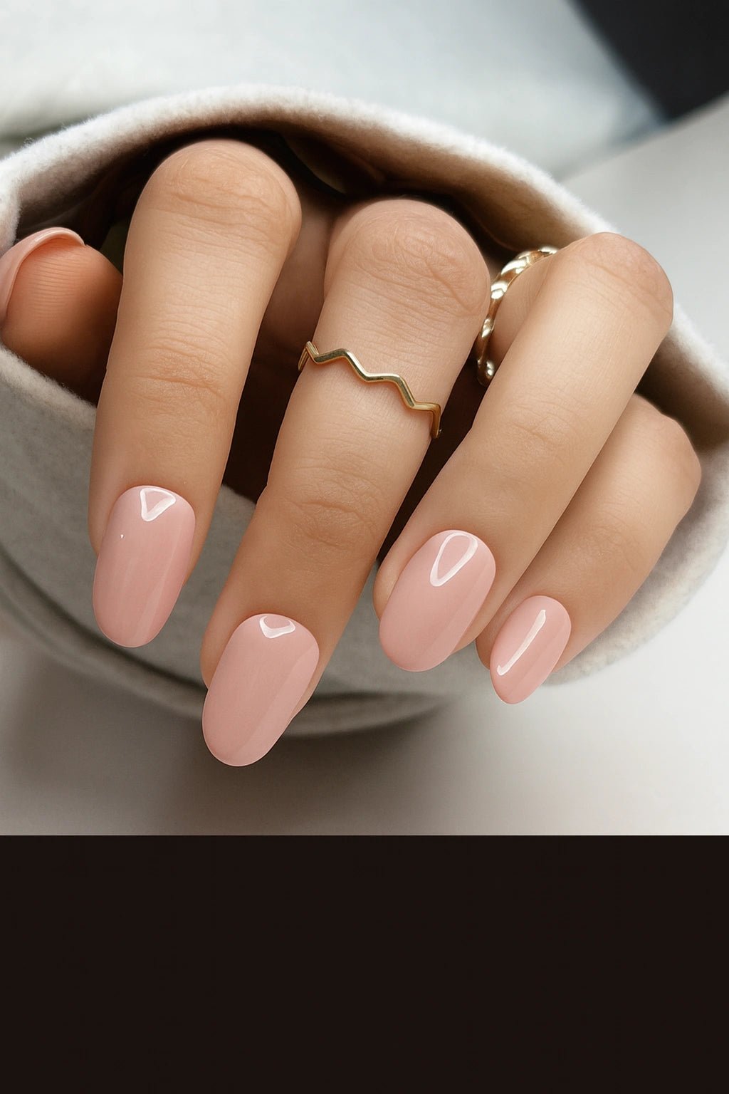 Close-up of a hand with nude short round nails and a gold ring on a neutral background