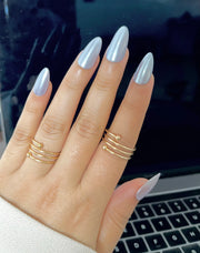 Hand with silver chrome long fake artificial nails in almond shape, in front of a blurred laptop keyboard. 