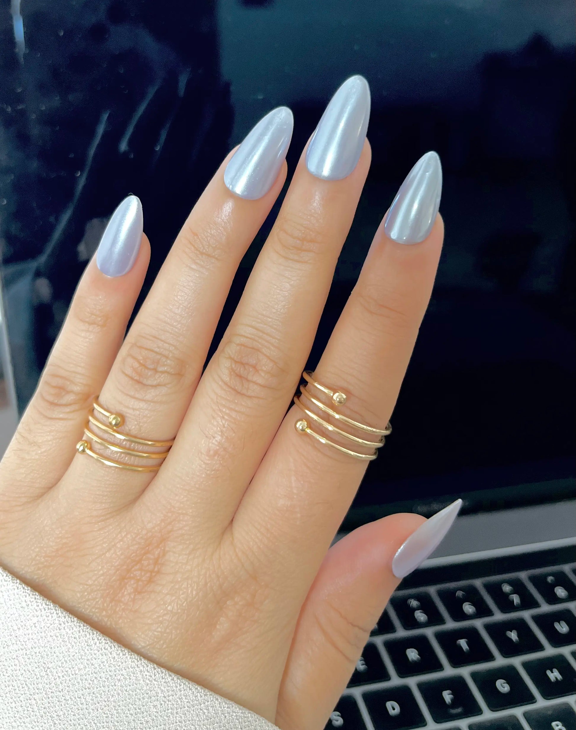Hand with silver chrome long fake artificial nails in almond shape, in front of a blurred laptop keyboard. 